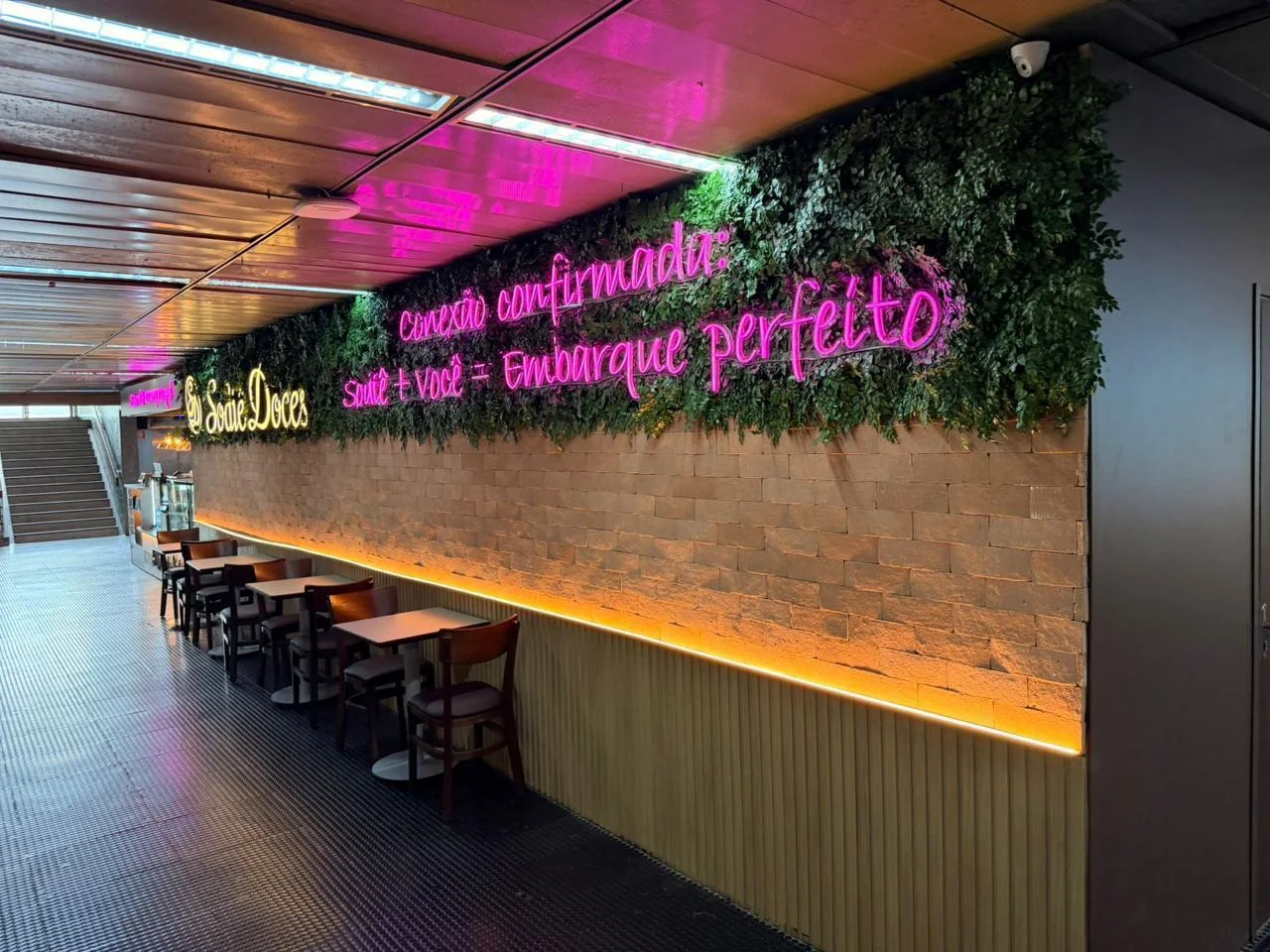 Sodiê Doces — área de consumo em aeroporto com jardim e comunicação em neon